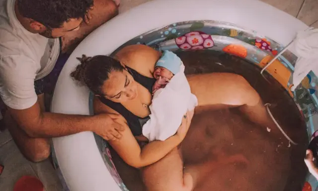 En nyfödd bebis vilar i sin mammas famn i ett födelsekar. Pappan stöttar dem båda. En lycklig stund för familjen som väntade sitt andra barn.