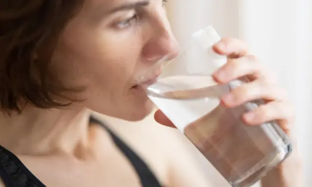Kvinna dricker vatten för att lindra muntorrhet, en potentiell biverkning av cancerbehandling.