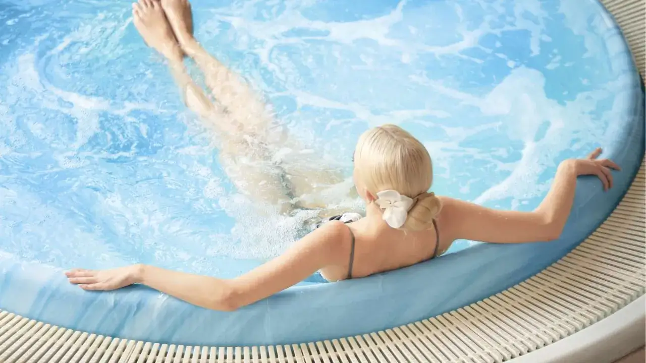 En gravid kvinna njuter av ett bubblande jacuzzi. Vattnet &auml;r klart och bl&aring;tt, och hon har en vit blomma i h&aring;ret.