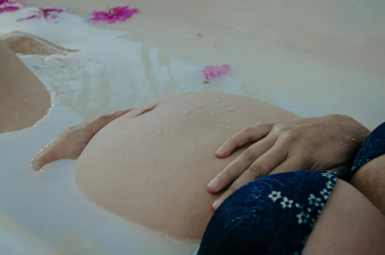 En gravid mage vilar i ett bad med blommor. En lugn stund f&ouml;r den som &auml;r basta gravid.