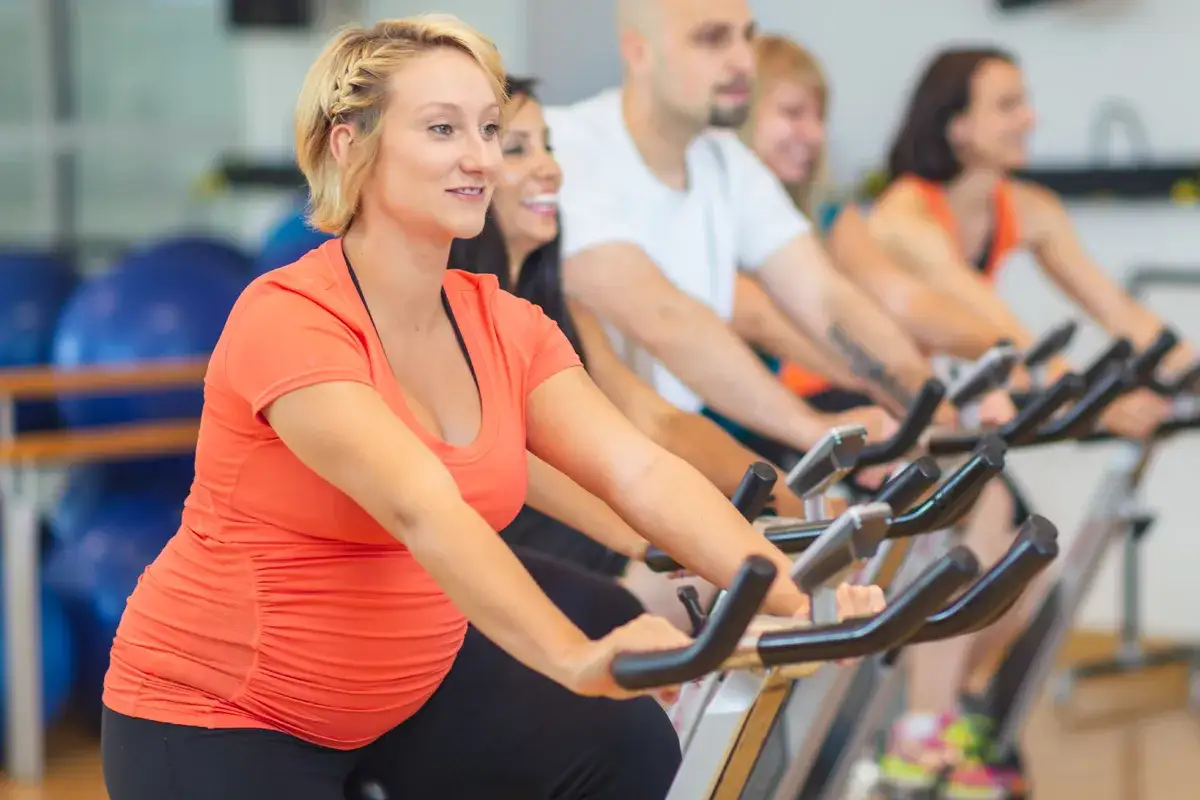 En glad, spinning gravid kvinna tränar på en motionscykel i ett gym.