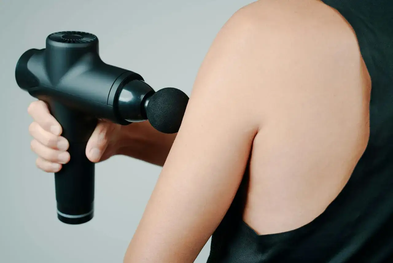 En hand h&aring;ller en svart massagepistol mot en arm. Kan vara anv&auml;ndbar f&ouml;r massage under graviditet.