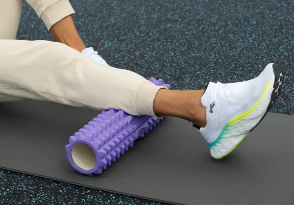 Person använder en lila foam roller rygg för att stretcha benet på en träningsmatta.