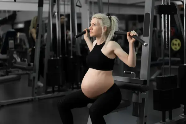 En **spinning gravid** tränar på gym. Hon sitter på en träningsmaskin och drar i ett handtag.